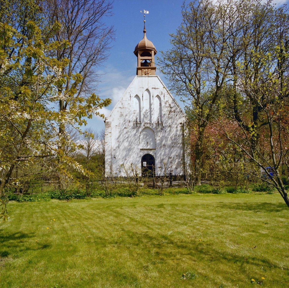 Simple white church with a wooden bell tower in the countryside.