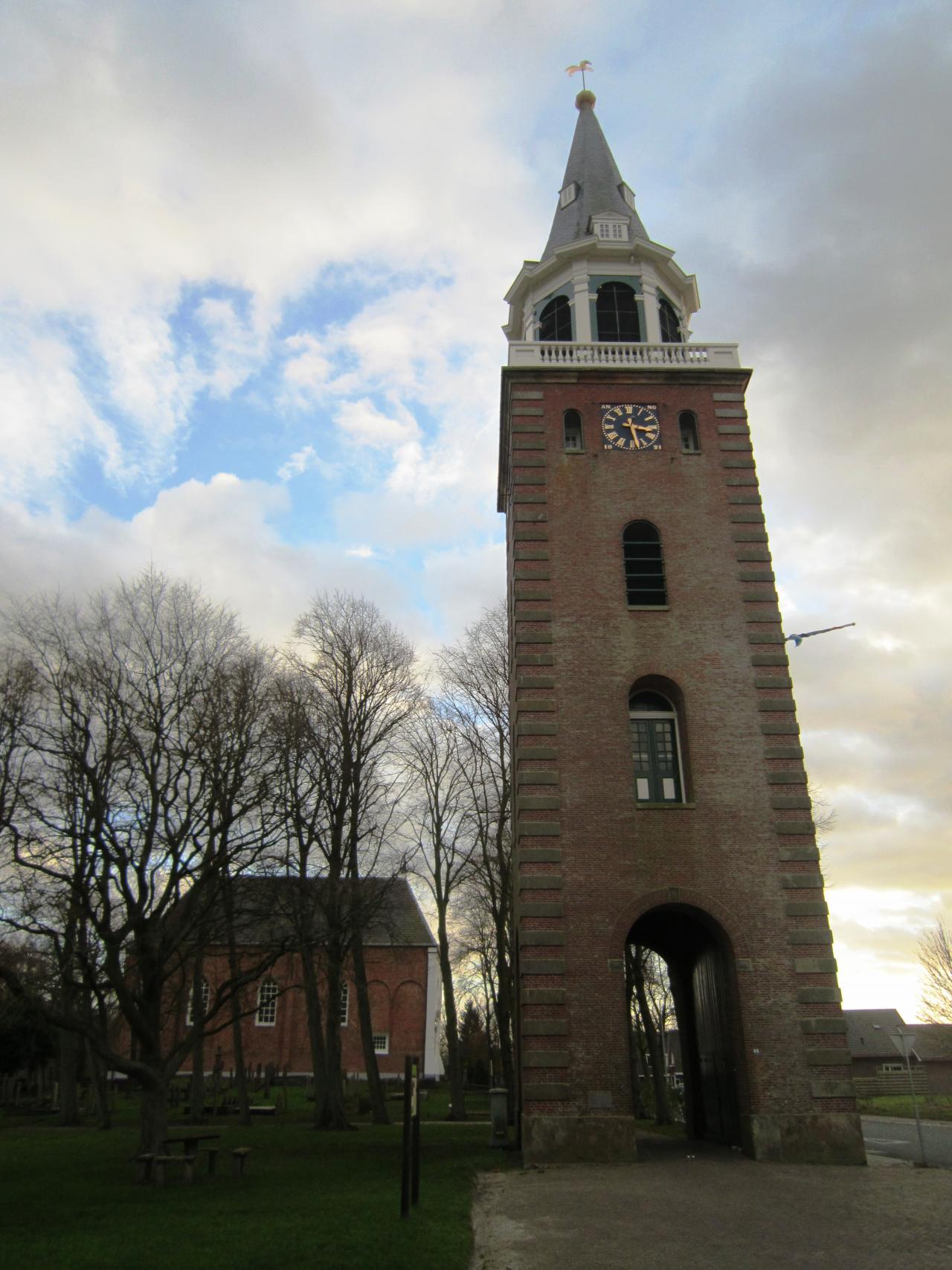 Bell tower witha pointed roof in the foreground and church in the distance