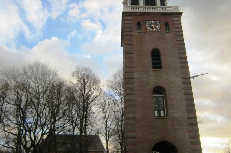 Bell tower witha pointed roof in the foreground and church in the distance
